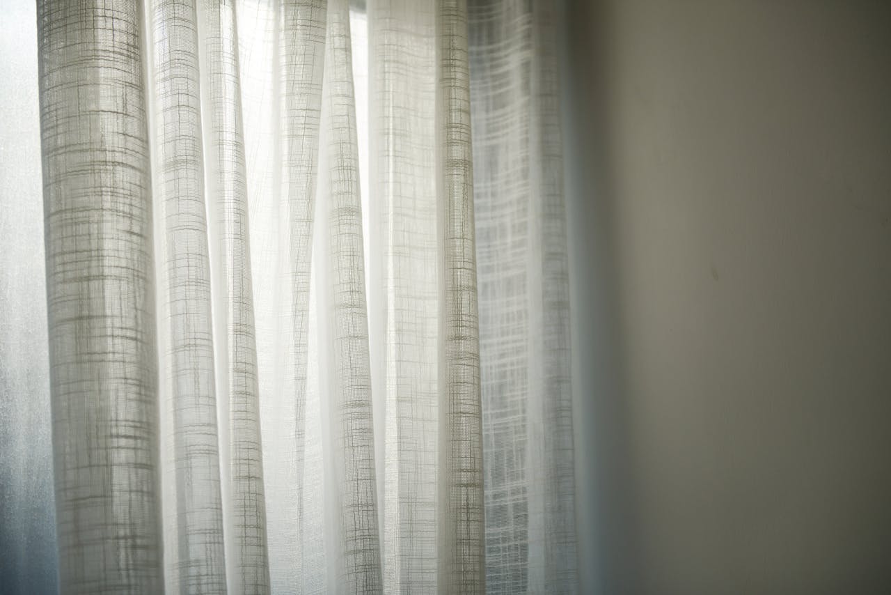 Sheer white curtains gently lit by daylight create subtle shadows on the wall.